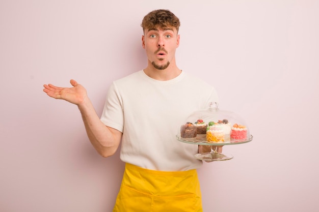 Młody fajny mężczyzna wyglądający na zaskoczonego i zszokowany z opadniętą szczęką, trzymający koncepcję domowych ciastek obiektu