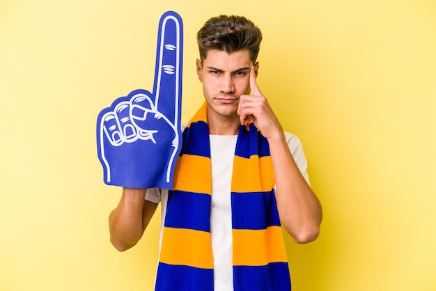 Młody fan sportu mężczyzna na białym tle na żółtym tle wskazując świątynię palcem, myśląc, skupiony na zadaniu.