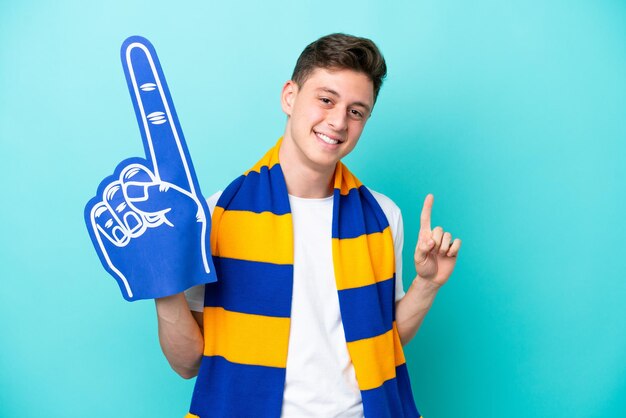 Młody fan sportu na białym tle na niebieskim tle pokazujący i unoszący palec na znak najlepszych