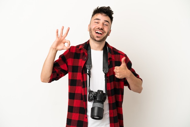 Młody fotograf kaukaski mężczyzna na białym tle pokazując znak ok i gest kciuka w górę