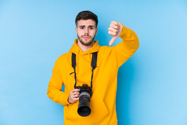 Młody fotograf kaukaski mężczyzna na białym tle przedstawiający gest niechęci, kciuki w dół. Pojęcie sporu.