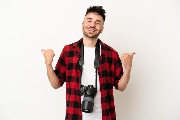 Młody fotograf kaukaski mężczyzna na białym tle z kciukiem w górę gestem i uśmiechem