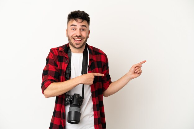 Młody fotograf kaukaski mężczyzna na białym tle zaskoczony i wskazujący bok