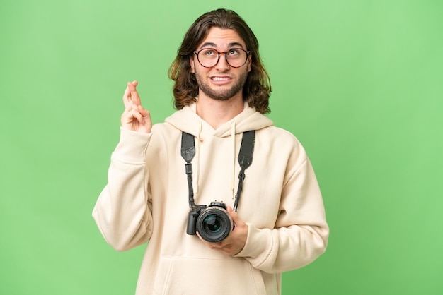 Młody fotograf mężczyzna na odosobnionym tle ze skrzyżowanymi palcami i życząc wszystkiego najlepszego