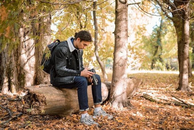 Młody fotograf przyrody siedzący na logu w lesie, oglądający zdjęcia