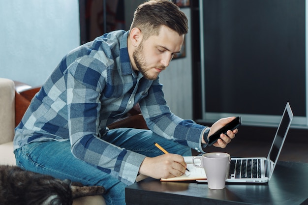 Młody freelancer pisze w zeszycie podczas pracy z domu