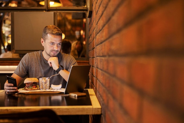 Zdjęcie młody freelancer siedzący w restauracji z tabletem i komórką podczas przerwy obiadowej