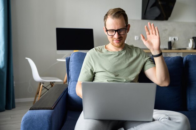 Młody freelancer w okularach używający laptopa do połączenia wideo