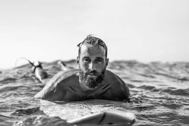 Zdjęcie młody hipster człowiek pływający na desce surfingowej do wody morskiej, czekając na dużą falę fajny facet bawiący się w sportach ekstremalnych koncepcja przygody i wolności podczas uprawiania sportów wodnych skup się na jego twarzy