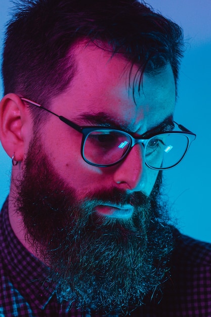 Młody hipster mężczyzna w niebieskich okularach światła patrząc od aparatu z poważną twarzą w kolorach niebieskim i różowym