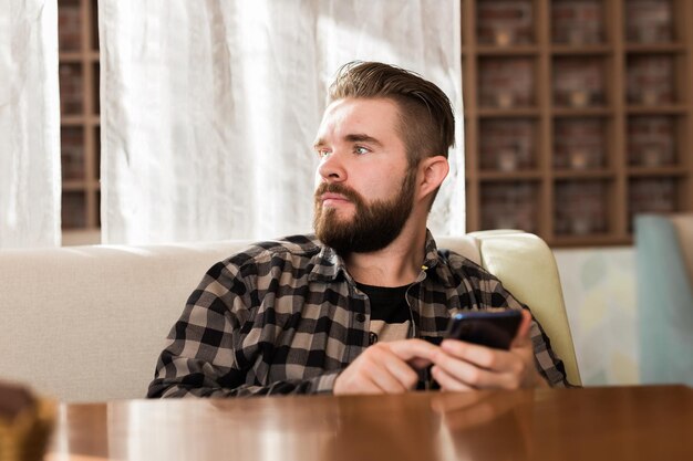 Młody hipster patrzący na wiadomości z sieci społecznościowych czytany przez smartfon w czasie wolnym w kawiarni