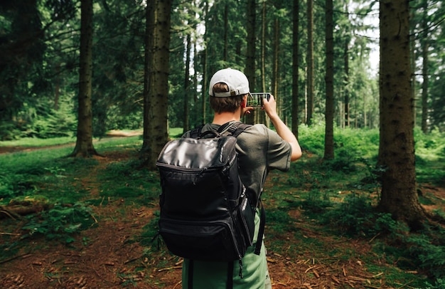 Młody hipster z plecakiem na plecach zatrzymał się, aby sfotografować piękny krajobraz