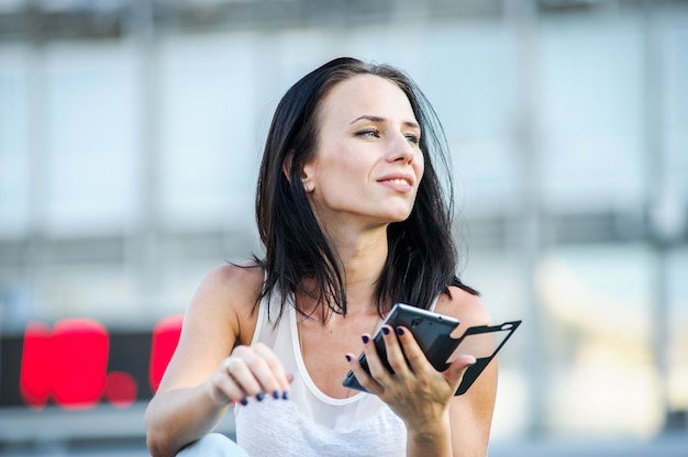Młody i piękny nowoczesny biznes kobieta pozuje na zewnątrz z inteligentnym telefonem.