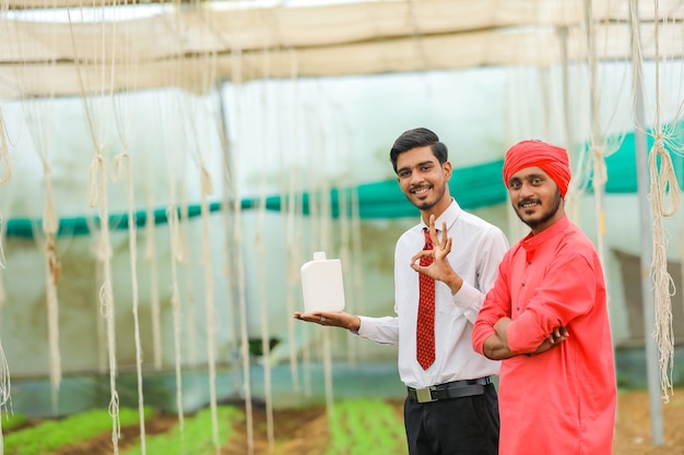 Młody indyjski agronom i rolnik pokazując butelkę w szklarni