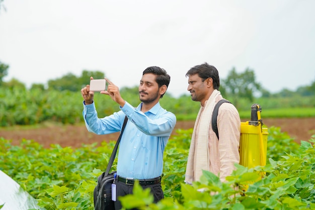 Młody indyjski agronom lub bankier pokazujący pewne informacje rolnikowi w smartfonie w dziedzinie rolnictwa.