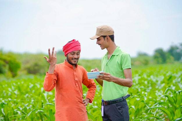 Młody indyjski bankier lub agronom pokazujący niektóre szczegóły rolnikom w smartfonie na polu rolnictwa.