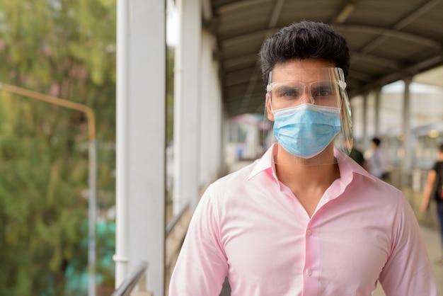 Młody indyjski biznesmen noszenie maski i osłony twarzy przy kładce
