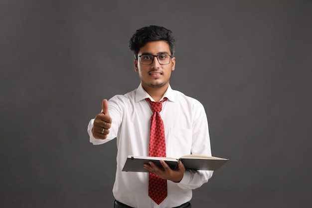Młody indyjski człowiek sukcesu w biznesie lub wykonawczej w okularach i czytanie książki na ciemnym tle.