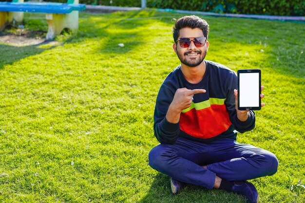 Młody indyjski mężczyzna używający smartfona w parku