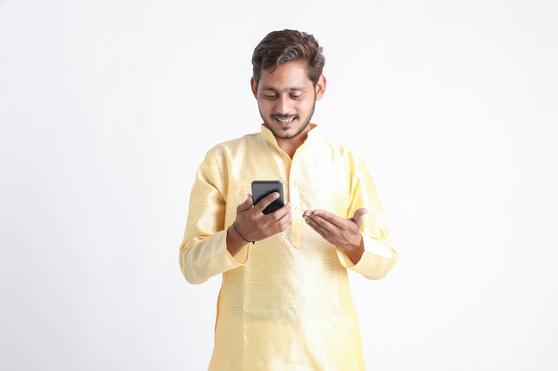 Młody indyjski mężczyzna w tradycji noszenia i używania smartfona na białej ścianie