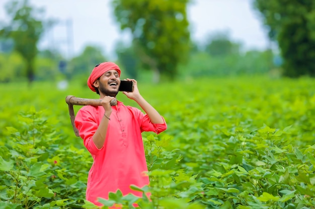 Młody indyjski rolnik za pomocą smartfona w zielonym polu bawełny
