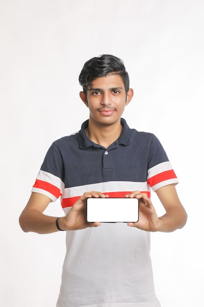 Młody indyjski student college'u pokazuje ekran smartfona na białym tle.