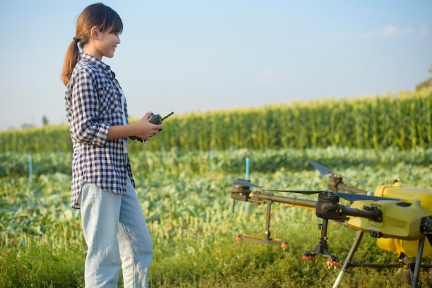 Młody inteligentny rolnik kontrolujący opryskiwanie dronem nawozów i pestycydów na polach uprawnych