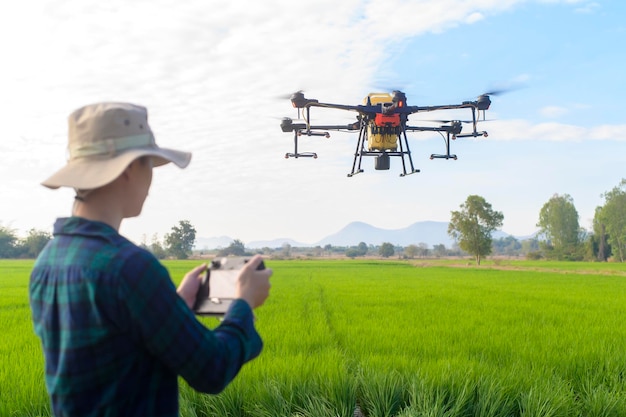 Młody inteligentny rolnik kontrolujący opryskiwanie dronem nawozów i pestycydów na polach uprawnych