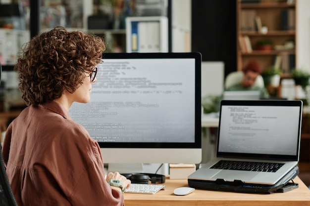 Młody inżynier patrzący na ekran laptopa z zakodowanymi danymi