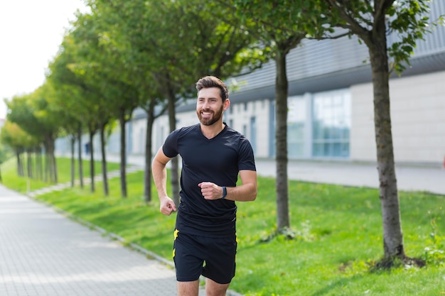 Młody kaukaski brodaty człowiek szczęśliwy biegacz jogging ulicą na tle miejskim parku miejskiego. Poranny jogging. Aktywny zdrowy styl życia fitness. Trening sportowy na świeżym powietrzu. Trening sportowca bieganie ćwiczenie