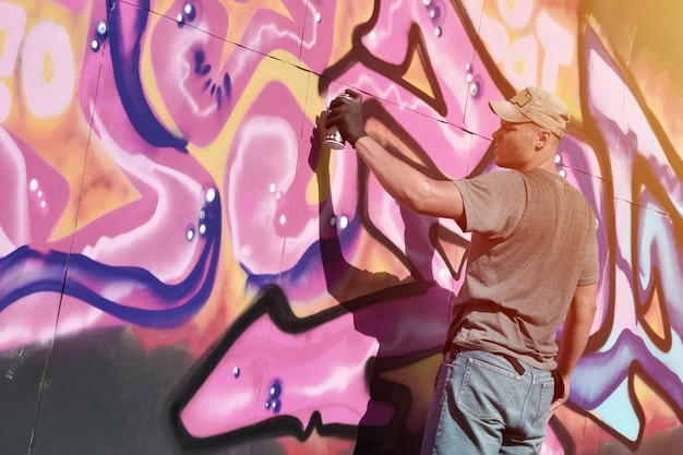 Młody kaukaski męski artysta graffiti rysujący duży obraz uliczny w odcieniach niebieskiego i różowego