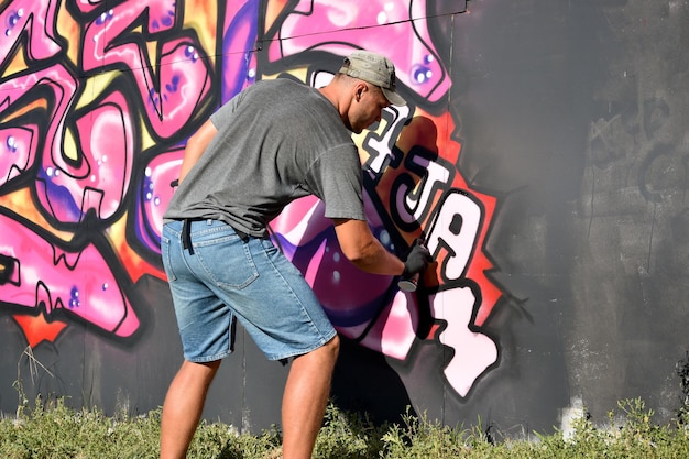 Młody kaukaski męski artysta graffiti rysujący duży obraz uliczny w odcieniach niebieskiego i różowego