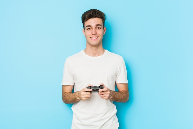 Młody kaukaski mężczyzna grający w gry wideo z kontrolerem do gier szczęśliwy, uśmiechnięty i wesoły.