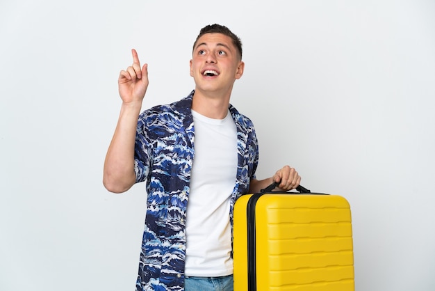 Młody kaukaski mężczyzna na białym tle na białej ścianie w wakacje z walizką podróżną i skierowaną w górę
