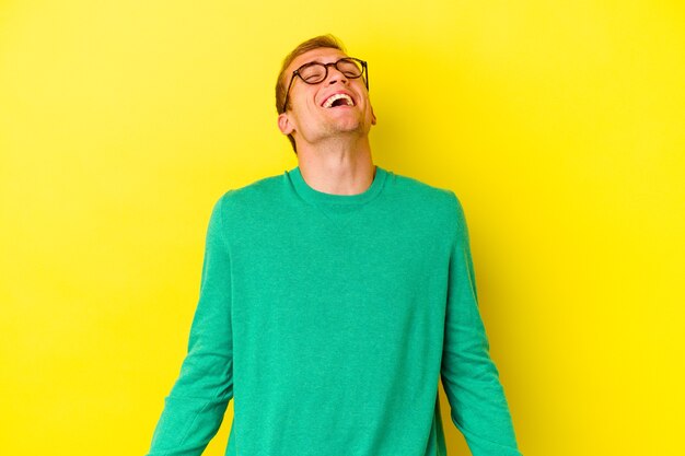 Młody kaukaski mężczyzna na białym tle na żółtej ścianie zrelaksowany i szczęśliwy, śmiejący się, wyciągnięta szyja, pokazująca zęby.