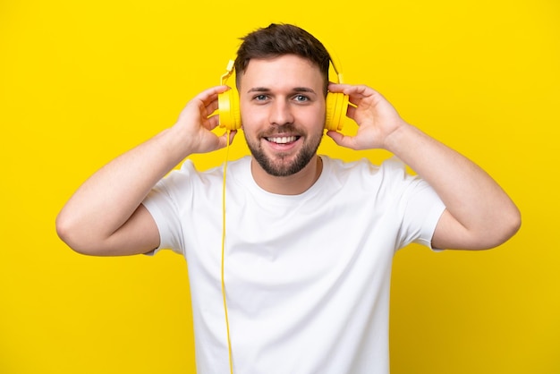 Młody kaukaski mężczyzna na żółtym tle słuchający muzyki