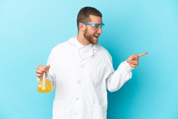 Młody kaukaski mężczyzna naukowy na białym tle na niebieskiej ścianie wskazując palcem w bok i prezentuje produkt