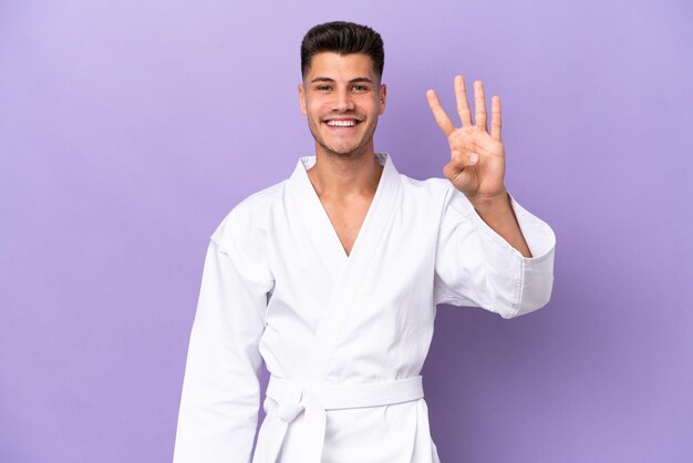 Młody kaukaski mężczyzna robi karate na fioletowym tle szczęśliwy i liczy cztery palcami