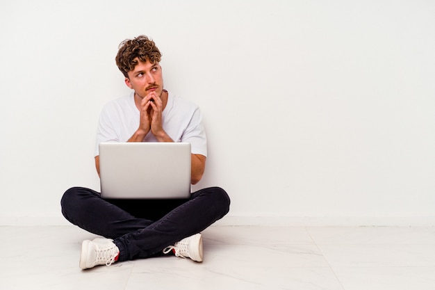 Młody kaukaski mężczyzna siedzi na podłodze, trzymając laptopa na białym tle, tworząc plan na uwadze, tworząc pomysł.