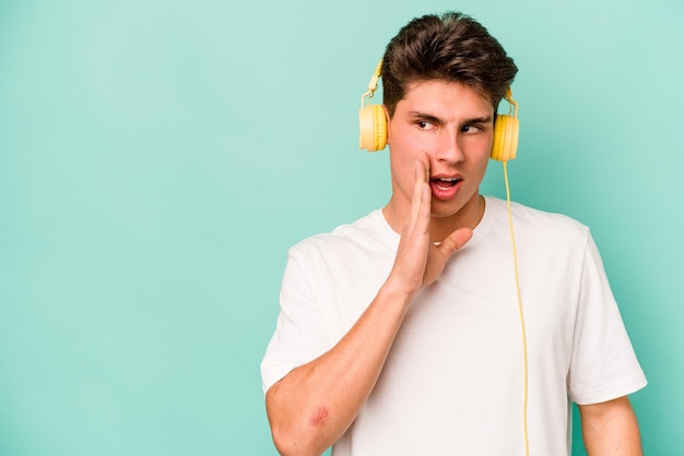 Młody kaukaski mężczyzna słuchający muzyki odizolowanej na niebieskim tle mówi tajne gorące wiadomości o hamowaniu i odwraca wzrok