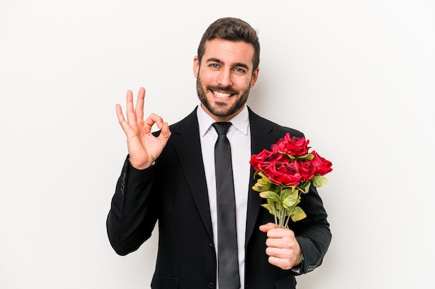 Młody kaukaski mężczyzna trzyma bukiet kwiatów na białym tle wesoły i pewny siebie, pokazując ok gest