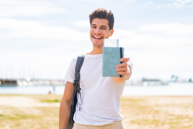 Młody kaukaski mężczyzna trzyma paszport na zewnątrz z radosnym wyrazem twarzy
