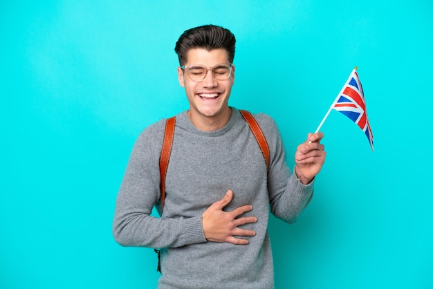 Młody Kaukaski Mężczyzna Trzymający Flagę Wielkiej Brytanii Na Białym Tle Na Niebieskim Tle Często Się Uśmiecha