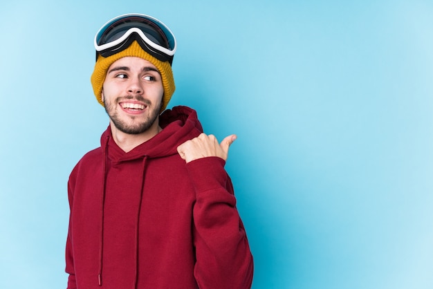 Młody kaukaski mężczyzna ubrany w ubrania narciarskie wskazuje kciuk palcem