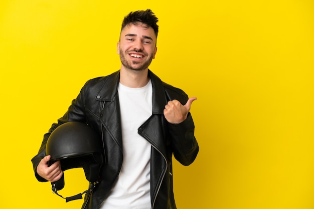 Młody kaukaski mężczyzna z kaskiem motocyklowym na białym tle na żółtym tle wskazujący na bok, aby zaprezentować produkt
