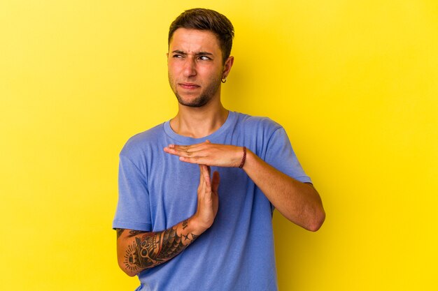 Młody kaukaski mężczyzna z tatuażami na białym tle na żółtym tle pokazując gest limitu czasu.
