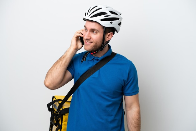 Młody kaukaski mężczyzna z termicznym plecakiem na białym tle prowadzi rozmowę z telefonem komórkowym z kimś