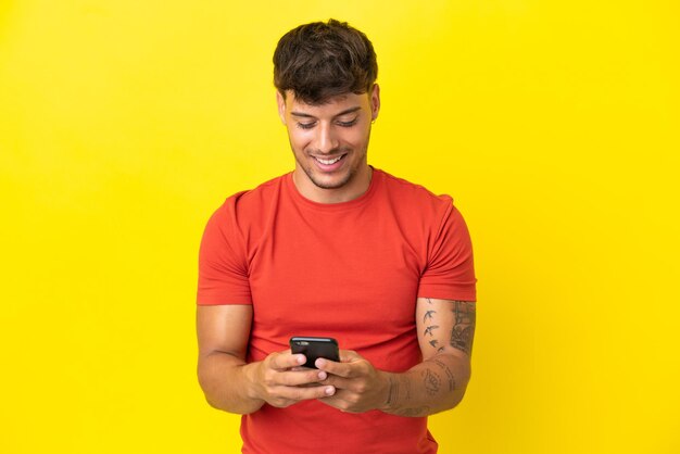 Młody kaukaski przystojny mężczyzna na białym tle na żółtym tle wysyła wiadomość za pomocą telefonu komórkowego