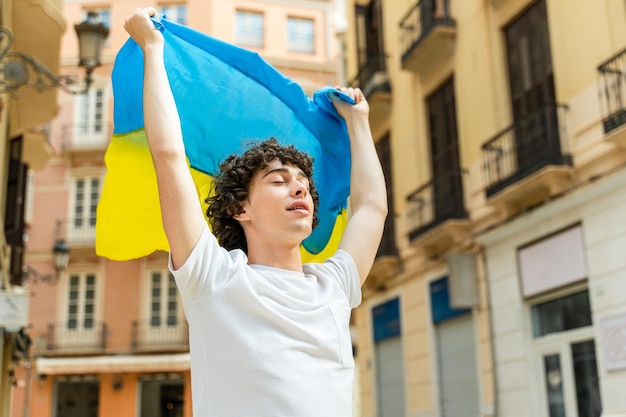 Młody Kędzierzawy Chłopiec Trzymający Ukraińską Flagę Na Ulicy I Uśmiechający Się Z Zamkniętymi Oczami