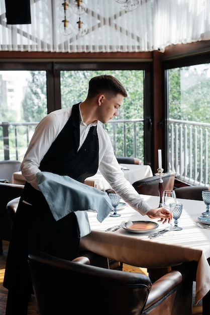 Młody kelner w stylowym mundurze zajmuje się obsługą stołu w pięknej restauracji dla smakoszy Restauracja na wysokim poziomie Obsługa stołowa w restauracji